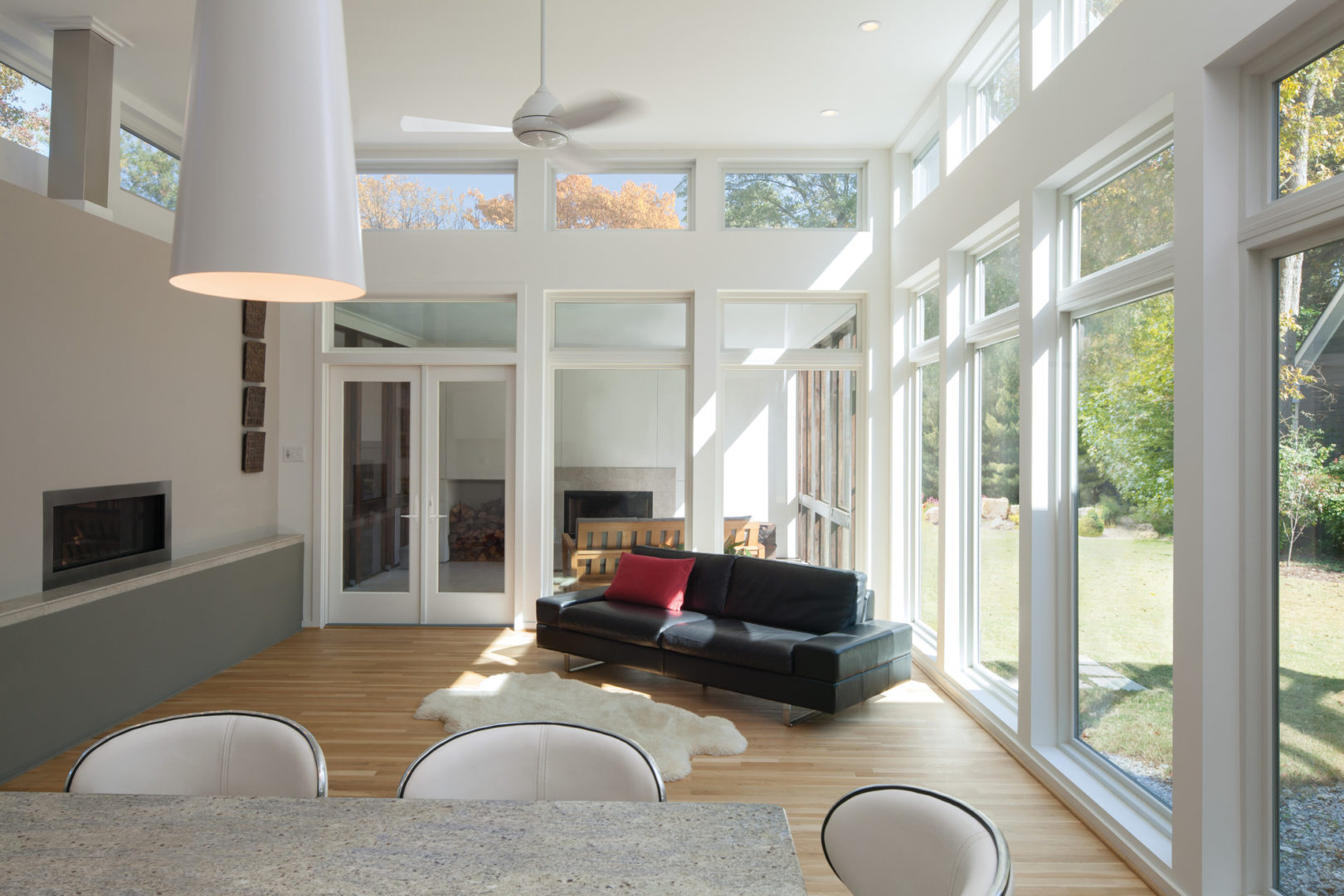 Living room with vaulted ceiling, wood flooring, and large energy-efficient windows overlooking scenic yard.