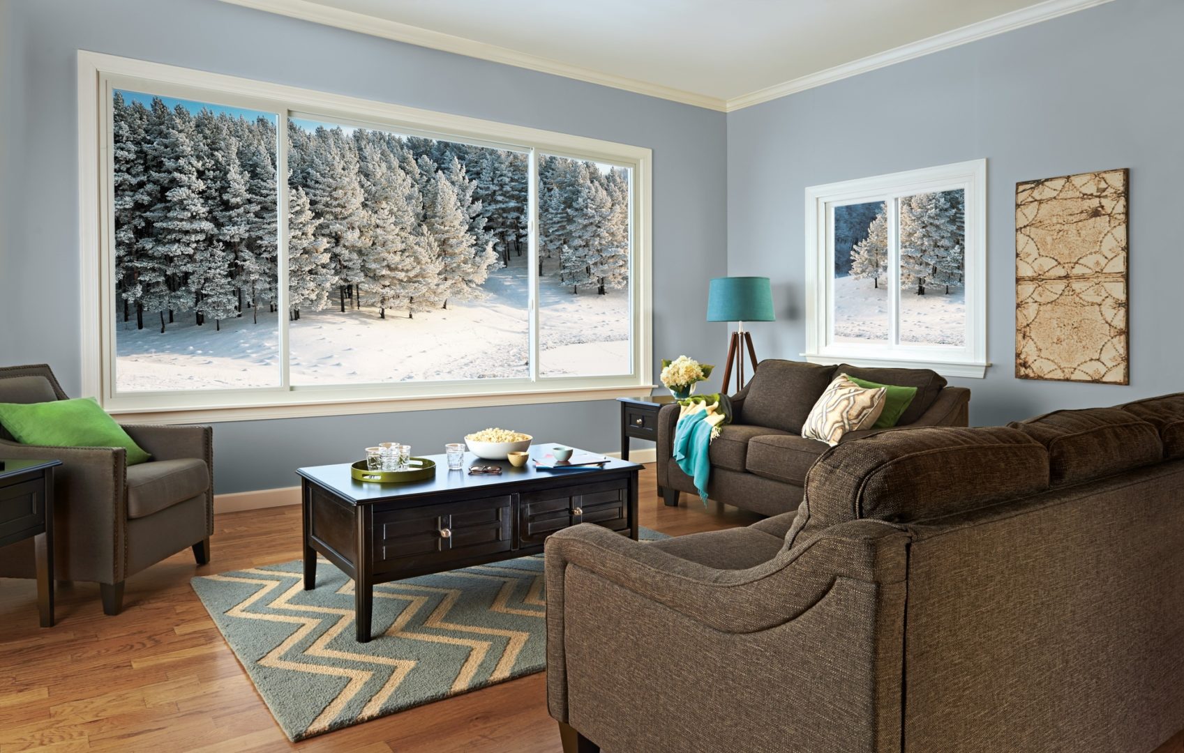 Cozy living room with wood flooring, plush brown seating, and large sliding windows overlooking frozen tundra.