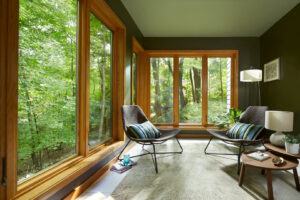 expansive picture windows in a cozy sitting room overlooking a wooded exterior
