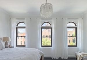 Clean white bedroom with black-framed windows looking out at the city