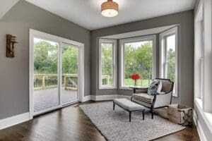 Beautiful sitting room with pale gray walls and windows and sliding glass door overlooking wood deck and backyard