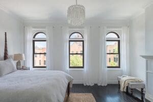 White bedroom with 3 single-hung windows in a row overlooking sunny day on the town